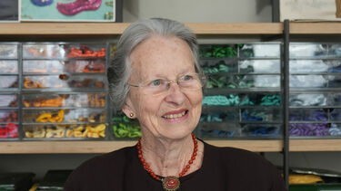 Headshot of a person wearing rimless glasses smiling in front of an array of colourful compartments.