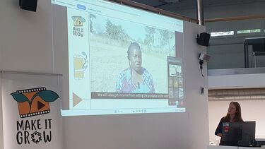 Pamela Richardson standing at a lectern giving a presentation which is projected onto the wall next to her