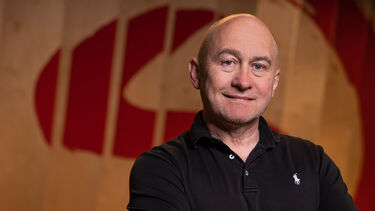Headshot of a bald person smiling in front of a red and white wall