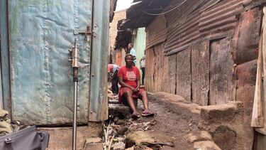 A local women in Mathare sitting down on a step next to a narrow pathway between two houses
