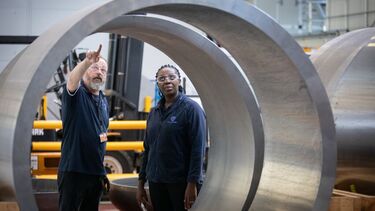A student and an instructor inspect a large metal cylinder in a factory setting