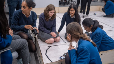 Schoolgirls work with current students in the robotic lab
