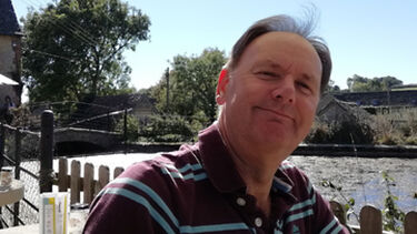 Steven Smart in a sunny riverside location, smiling warmly at the camera under a large parasol