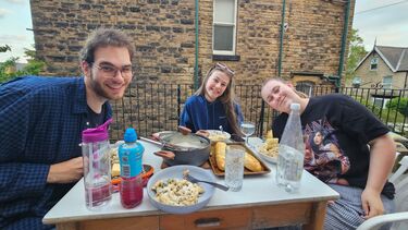 Three students on a roof terrace eating pasta. A typical Sheffield house in the background, stone, not brick