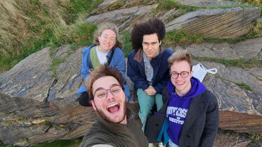 four students in an autumnal setting on a bolder in the Peak District