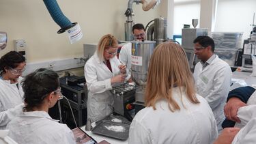 A group of researchers wearing lab coats taking part in a practical demonstration 