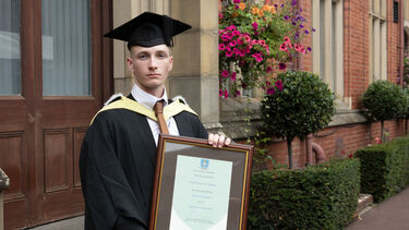 Joseph Shepherd posing in graduation gown with certificate 