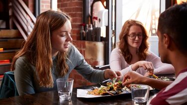 Three people sat at a table sharing food