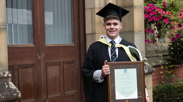Oliver Fox Fitzgerald posing in graduation gown with certificate 