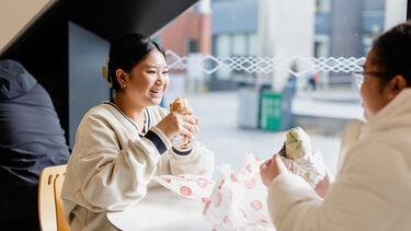 Two students sitting opposite each other and enjoying their burritos