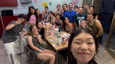 Mixed group of students in a student kitchen. Plenty of food on the table and they are dressed in summery clothes