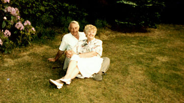 Arthur and Iris sitting together on a green lawn in middle age, and both smiling warmly at the camera