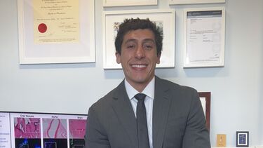 A person smiling at the camera sitting on a desk.