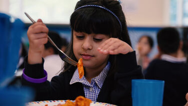 A girl in school uniform is holding pasta on her fork 