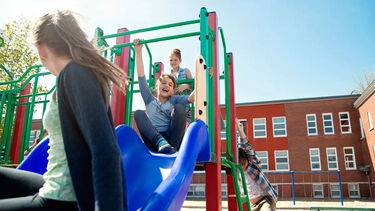 A group of children playing on a slide in a playground outside a school
