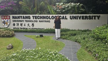 A female student stands outdoors in front of a sign that reads Nanyang Technological University and smiles towards the camera.