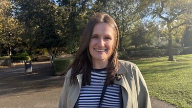 A person smiling at the camera with trees in the background.