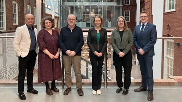 Six colleagues stand on a balcony area within the Engineering Heartspace and smile towards the camera.