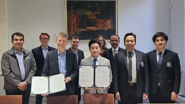 A group of nine colleagues stand in a row and smile towards the camera. Two members of staff in the centre each hold a signed document and present it towards the camera.