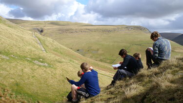 Geography students sat on bank in a national park making field notes