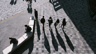 Birds' eye view of four students (and their shadows) walking across paving stones in the sunshine