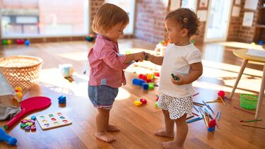 Two toddlers holding hands with lots of toys around them.