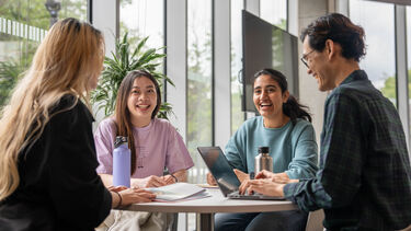 Four students working around a table smiling