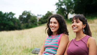 Two women sat on a bench in a field