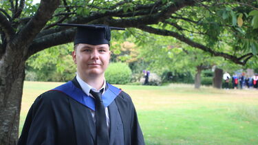 Ben Vass wearing graduation robes standing under a tree