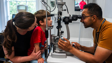 A male orthoptist checks a boy's vision while the boy sits on his mum's knee