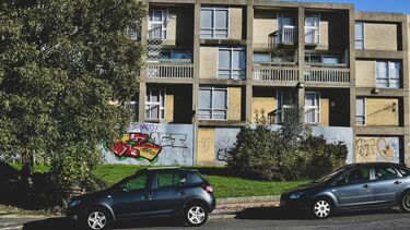 A photograph showing the exterior of a block of flats with graffiti