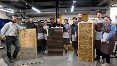 A group of people in a workshop standing with three wooden structures