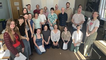 group of about 20 people some with papers in their hands smiling and singing