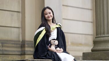 Alicia sits in a graduation gown holding a small teddy bear that wears a cap and gown