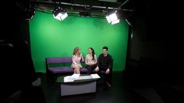 Three students sitting in front of a green screen on a purple sofa