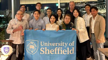 A group of Sheffield alumni in Japan posing for a picture with a University flag