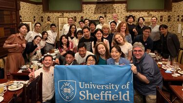 A group of Sheffield alumni in Japan posing for a picture with a University flag