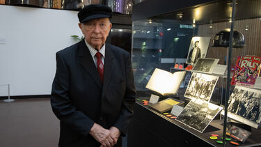 An elderly man stands next to a glass cabinet archive display