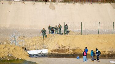 Border guards observing people across a barbed wire fence