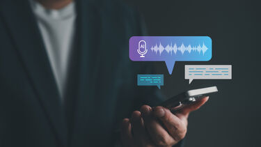 A close up shot of a man in a suit holding his phone and speaking to an AI assistant on loudspeaker