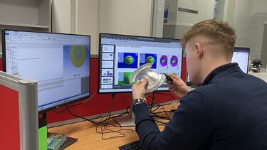 A man sits with his back to the camera, looking at a piece of circular metal