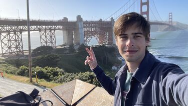 A young man stands in front of the Golden Gate Bridge