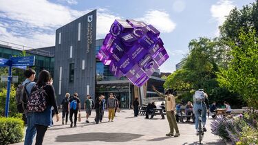 Students walking past Sheffield Students' Union and looking at a purple cube