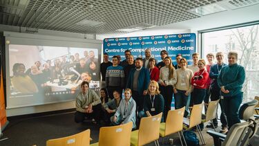 Group photo posed in front of a screen showing another team online