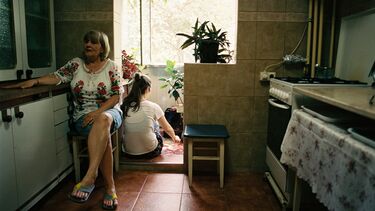 Two women sit in a kitchen with a balcony in the background