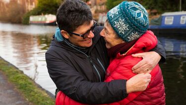 Two people embrace beside a canal with long boats