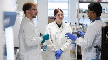 Three researchers wearing lab coats and PPE having a discussion
