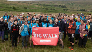 A large group of hikers in a field, holding a red banner that reads 'The Big Walk'