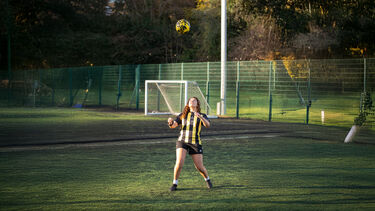 A girl stands in a field with a yellow football hovering above her head