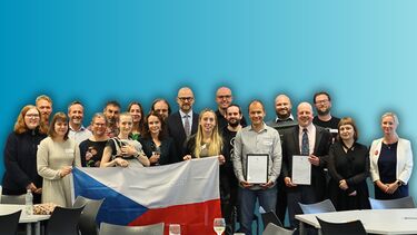 A large group of smiling people holding a Czech flag